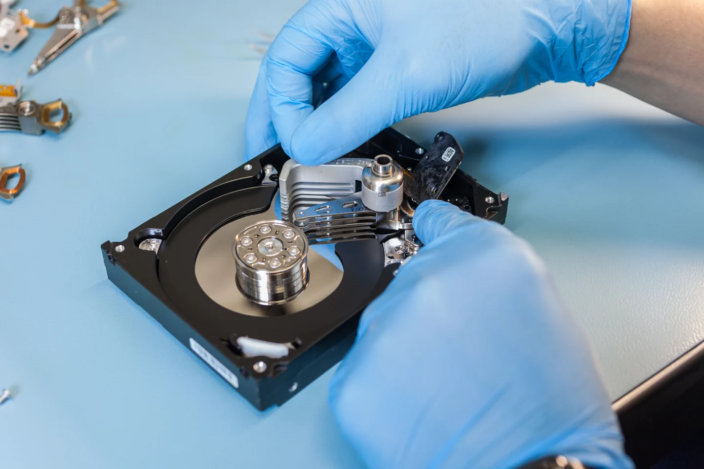 Руки специалиста в перчатках и открытый HDD на голубой рабочей поверхности